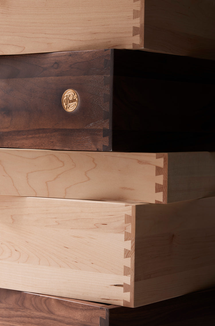Close-up detail shot of the dovetail joinery in a stack of drawers in light and dark wood varieties. The darkest drawer has Isla Porter's maker's mark on it.
