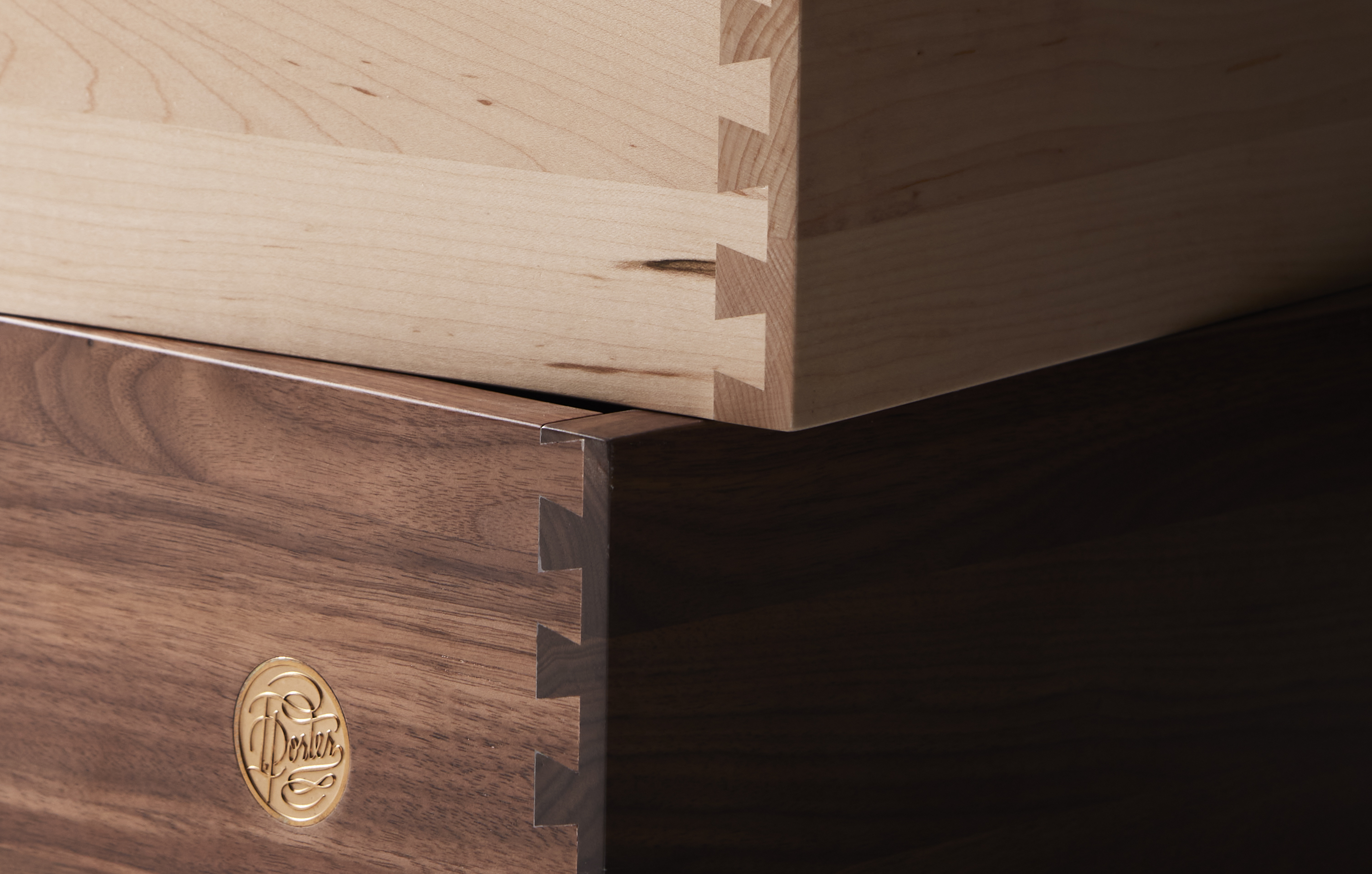 Close-up detail shot of the dovetail joinery in a stack of drawers in light and dark wood varieties. The darkest drawer has Isla Porter's maker's mark on it.