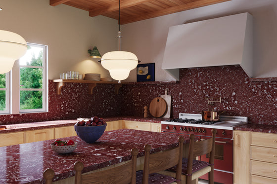 A modern kitchen featuring Isla Porter's Finn cabinets and Jove shelf in East Oak stain, Kipp range hood in "Coconuts" paint color, Burgundy Calcutta Marble countertops, brass hardware, and checkered floor tiles. A large window above the sink allows natural light to flood the space.