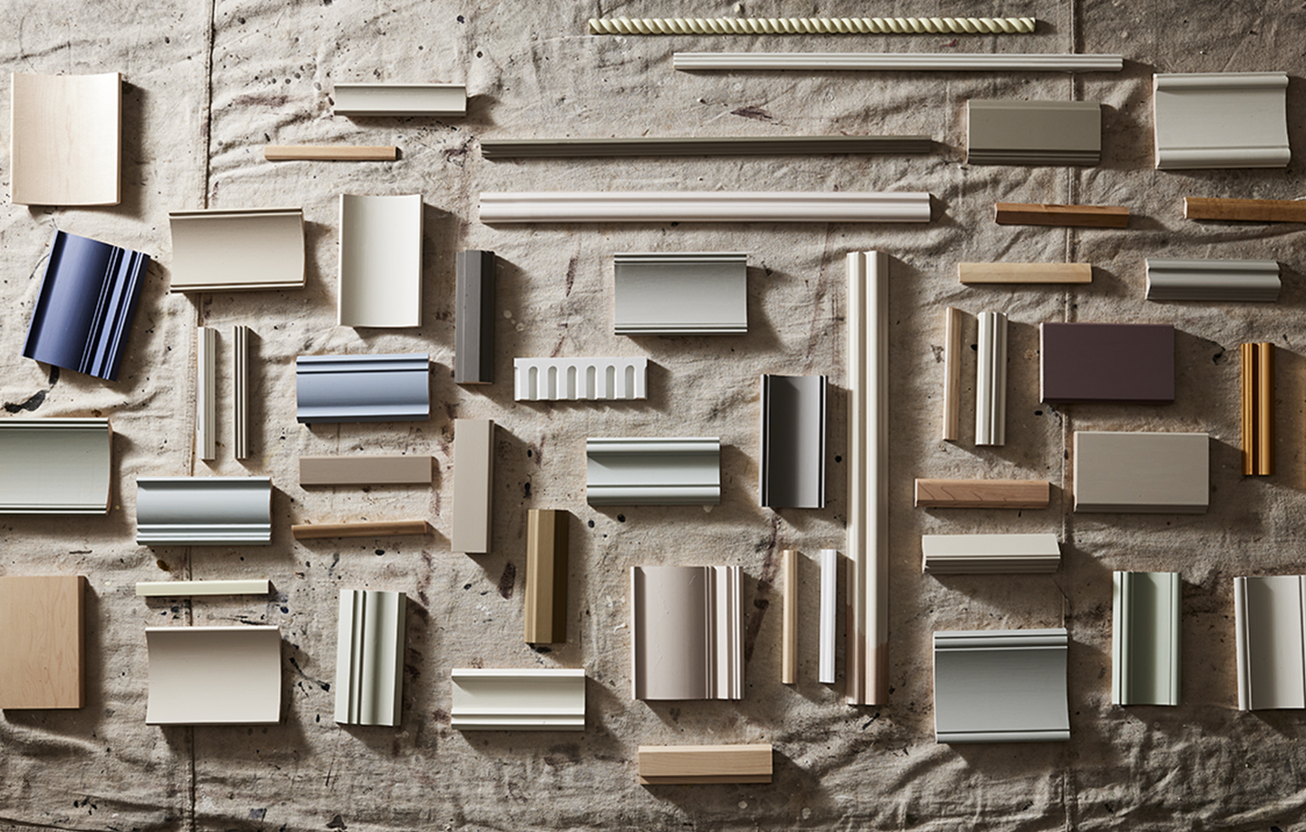 An array of trim samples arranged on a textured surface, displaying a range of trim styles and paint and wood stain hues.